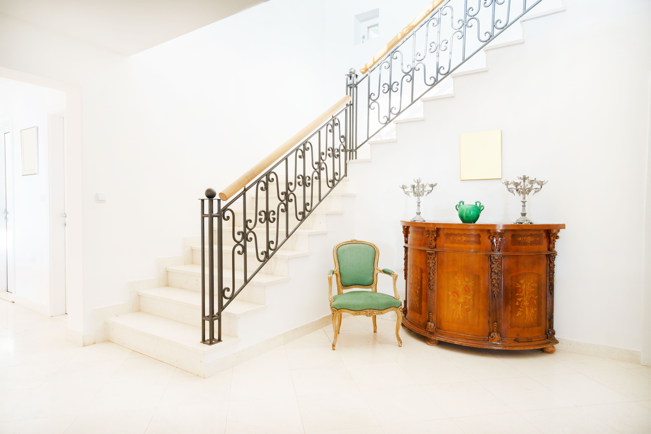 beautiful staircase with a chair and fine wood console sitting on the floor below the stairs.